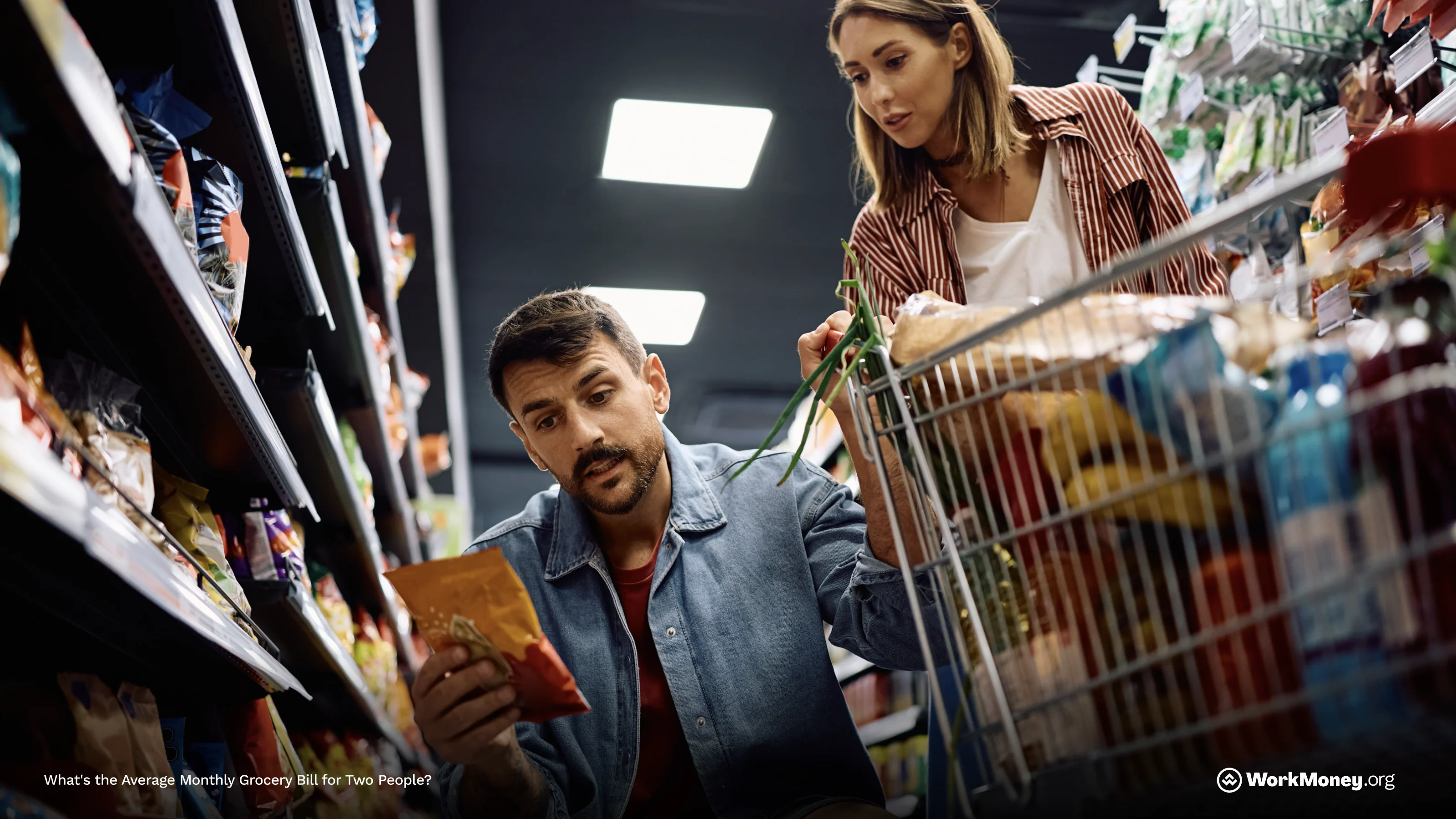 A couple shopping in a grocery store with a cart and looking at prices.