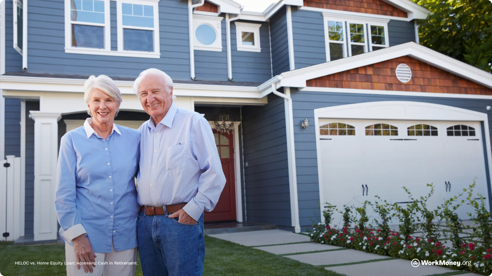 An older couple stand in front of their house smiling.