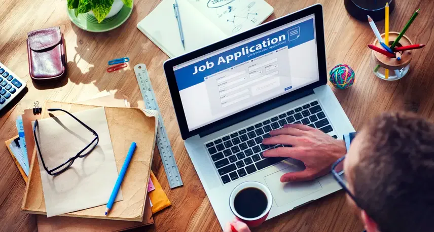 A person looking at a laptop on a desk with the words job application on the screen