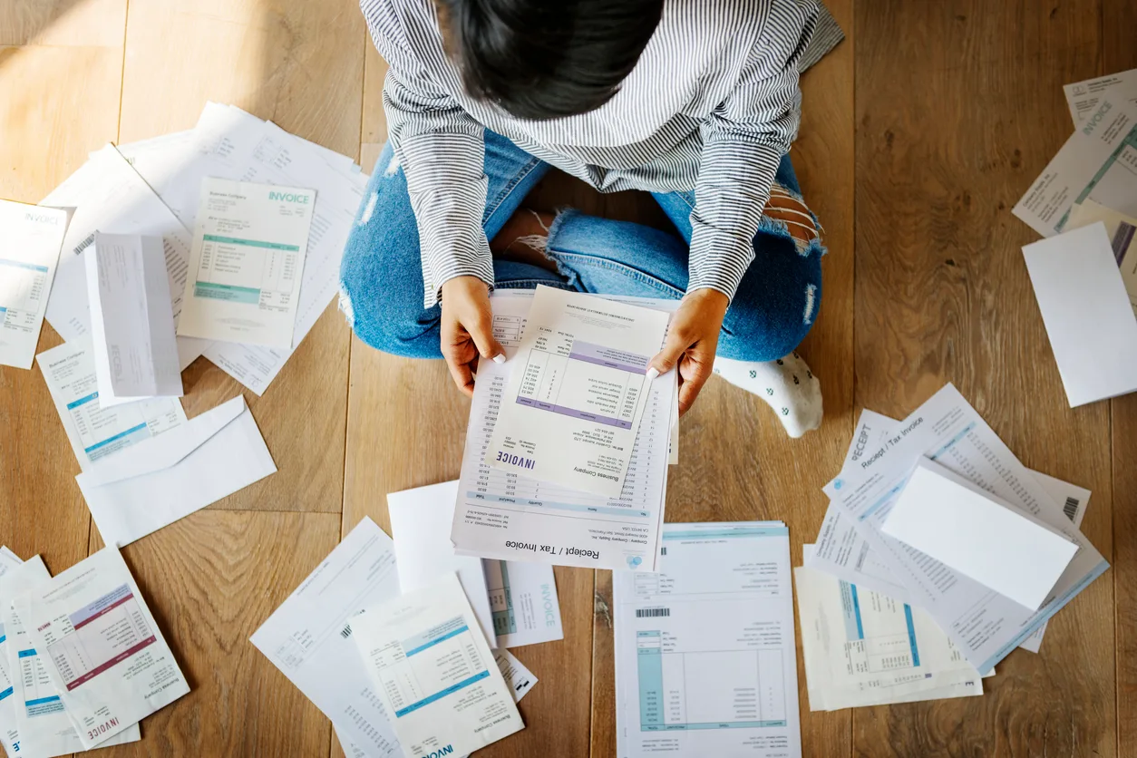 Person sitting on the floor surrounded by bills and invoices, reviewing documents—illustrating financial stress and efforts to manage or negotiate high bills.