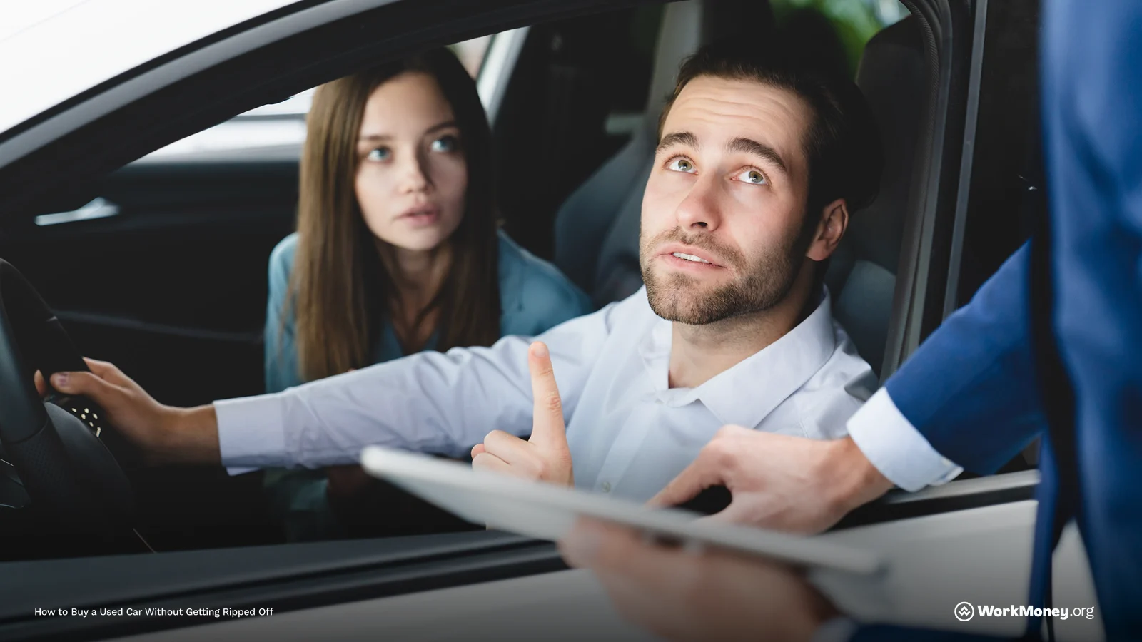 Man and woman sit in a car and speak to someone outside.