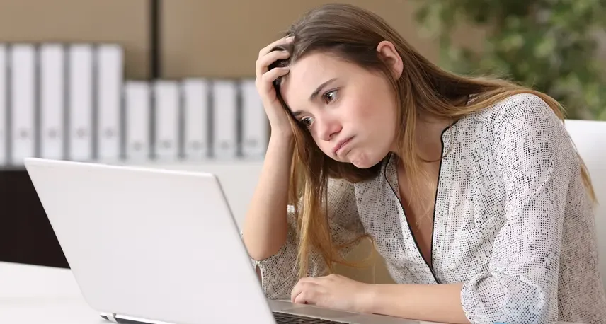 A woman with blond hair with her head in her hand looking at a laptop