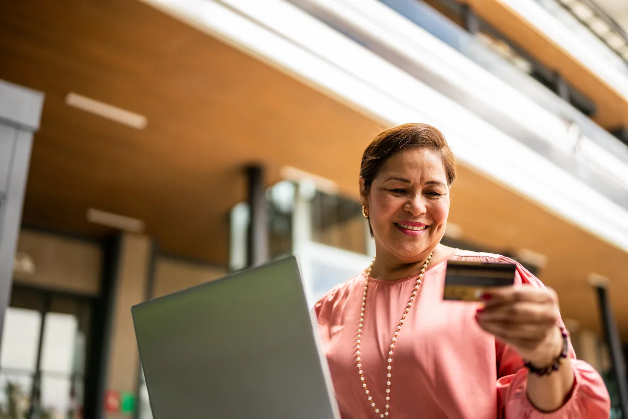 Foto de stock de mujer madura comprando en línea con una laptop al aire libre
