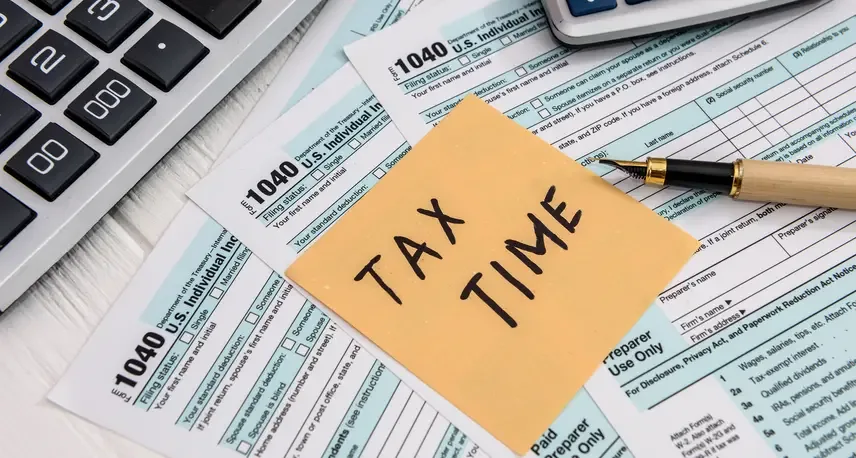 A yellow post it note that says tax time sitting on top of 1040 forms