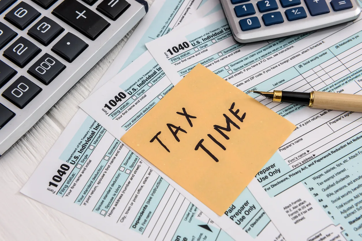 A yellow post it note that says tax time sitting on top of 1040 forms