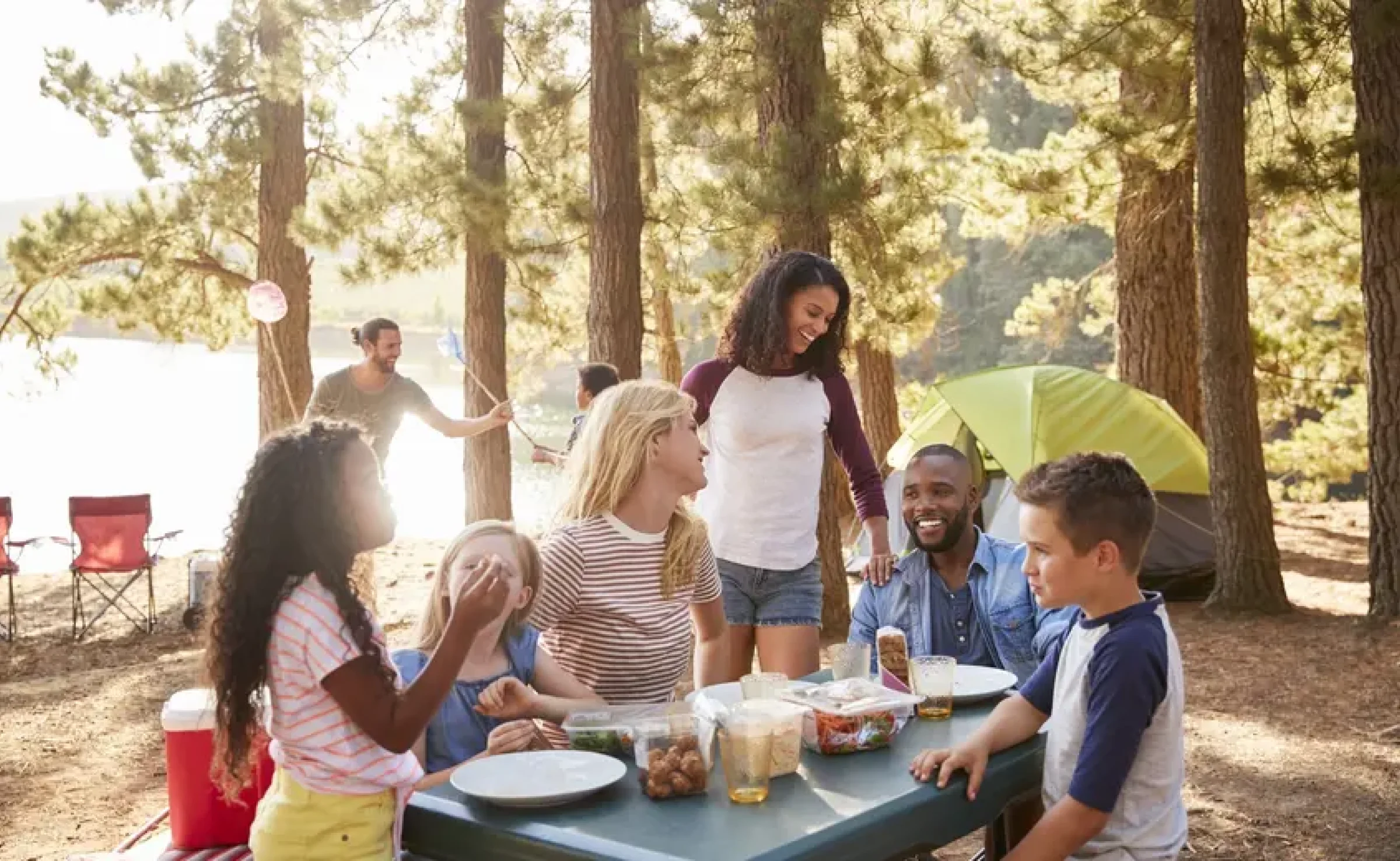 A group of people laughing while sitting at a picnic table outside by some trees