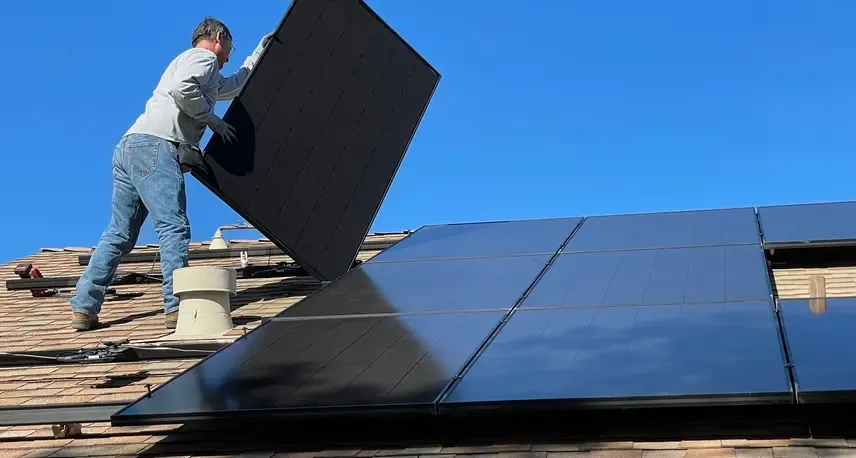 A person on a roof holding up a solar panel