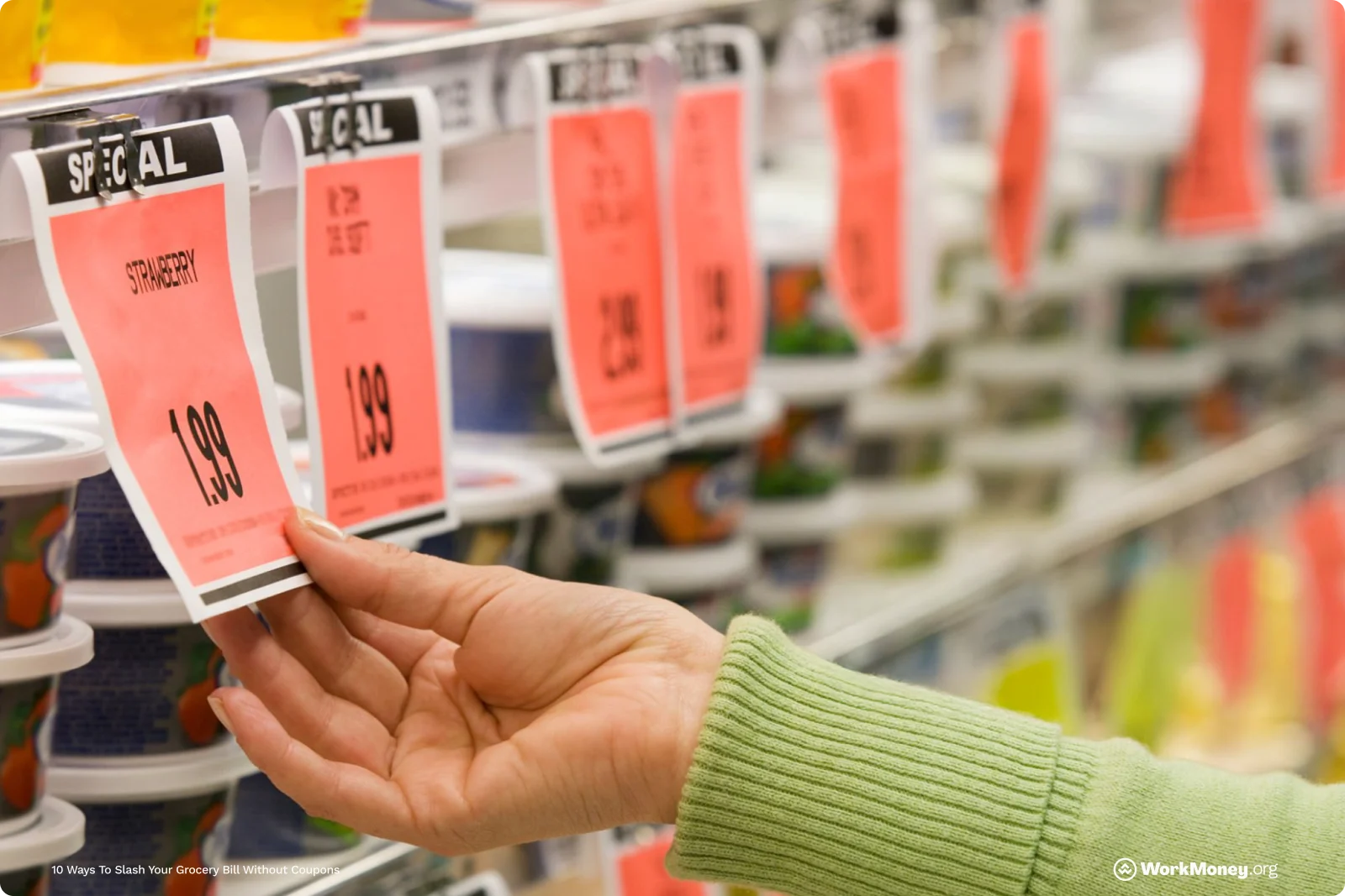 A person in a green sweater reaching for a red sale tag labeled “Strawberry $1.99” in a grocery store dairy aisle, with multiple discount tags and yogurt containers visible in the background.