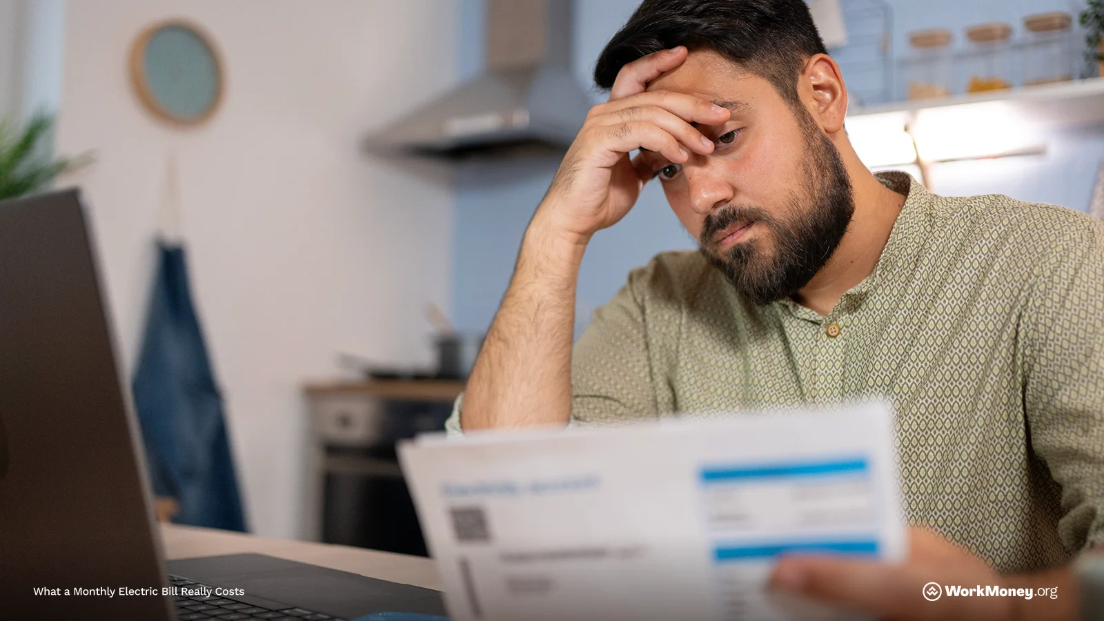 A man sits at a kitchen table looking stressed while reviewing a utility bill. He rests his forehead on one hand and holds the bill in the other, with a laptop open in front of him. The environment suggests concern over monthly expenses.