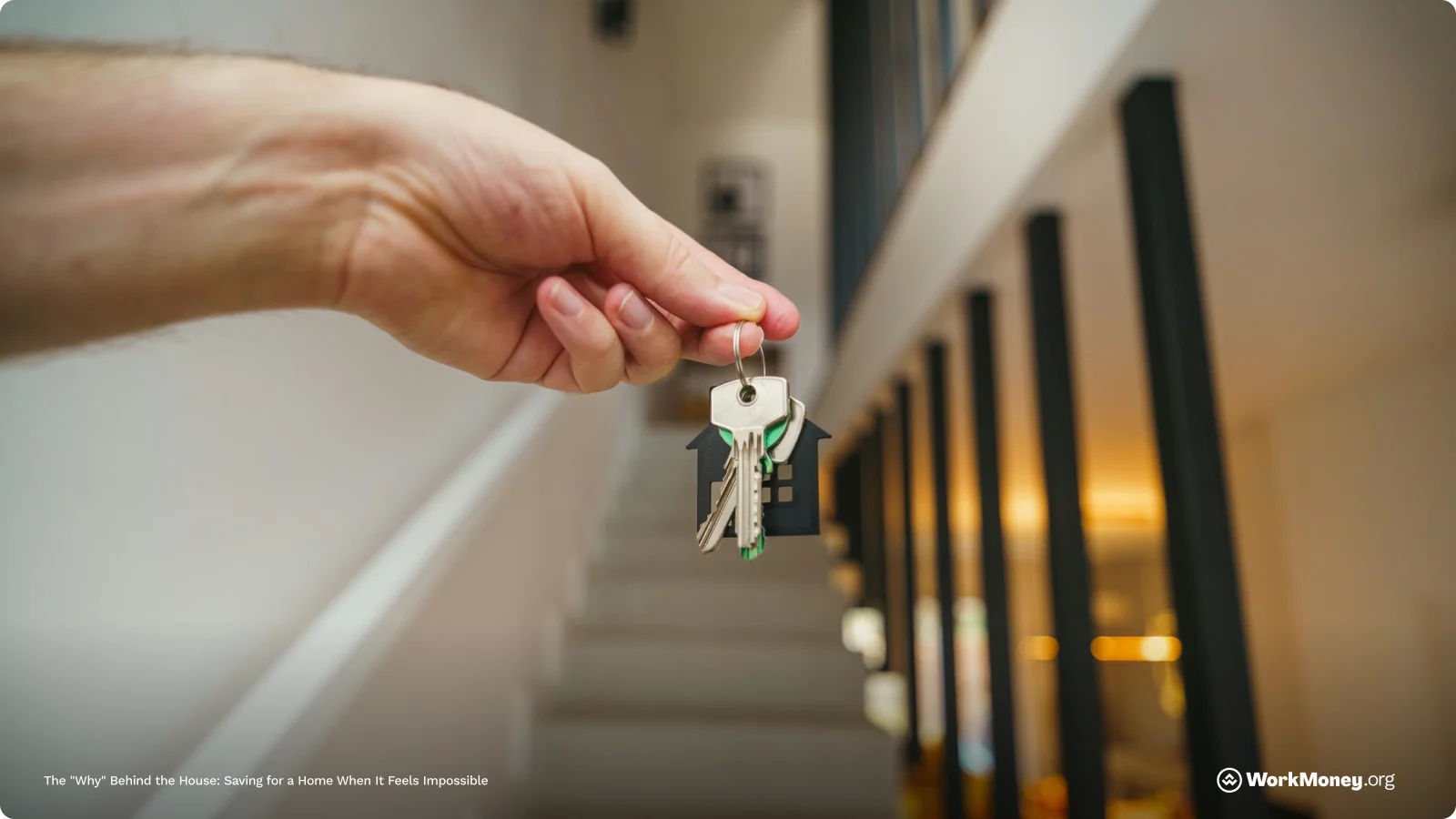 A hand holds house keys in front of some stairs