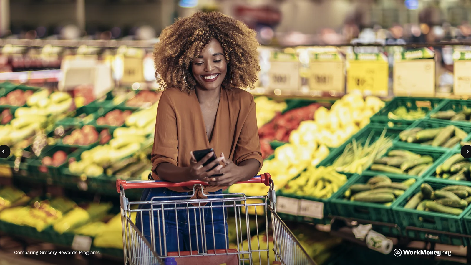 A woman checks her phone for grocery rewards or savings apps while shopping for fresh produce in a supermarket.