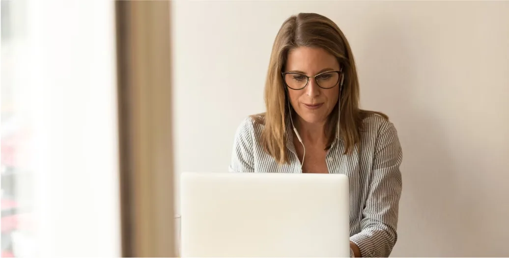 A woman with blonde hair and glasses looking down at a laptop