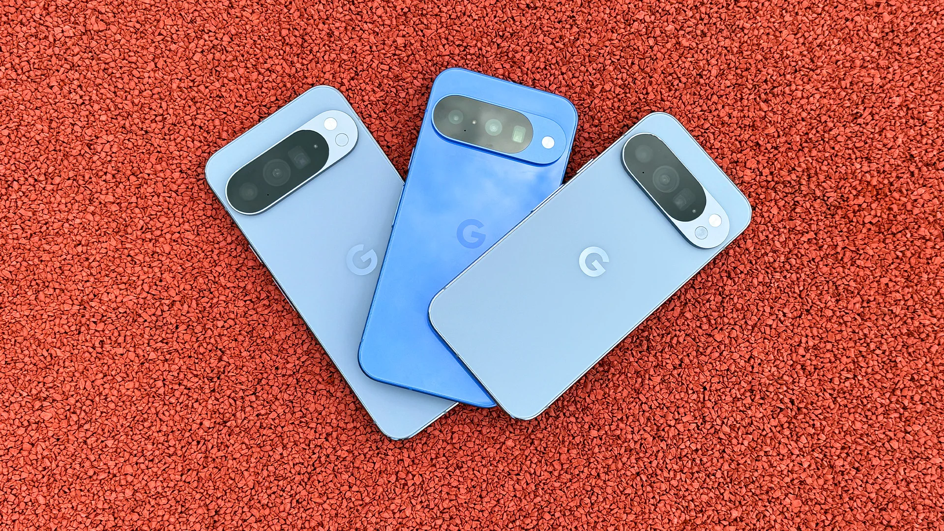 Tre blå mobiler med Googles logotyp ligger på en röd yta.