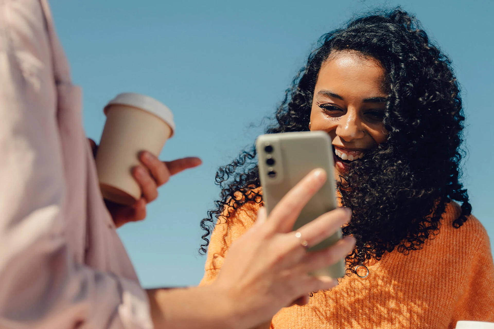 Leende kvinna tittar på mobil, vän med kaffekopp