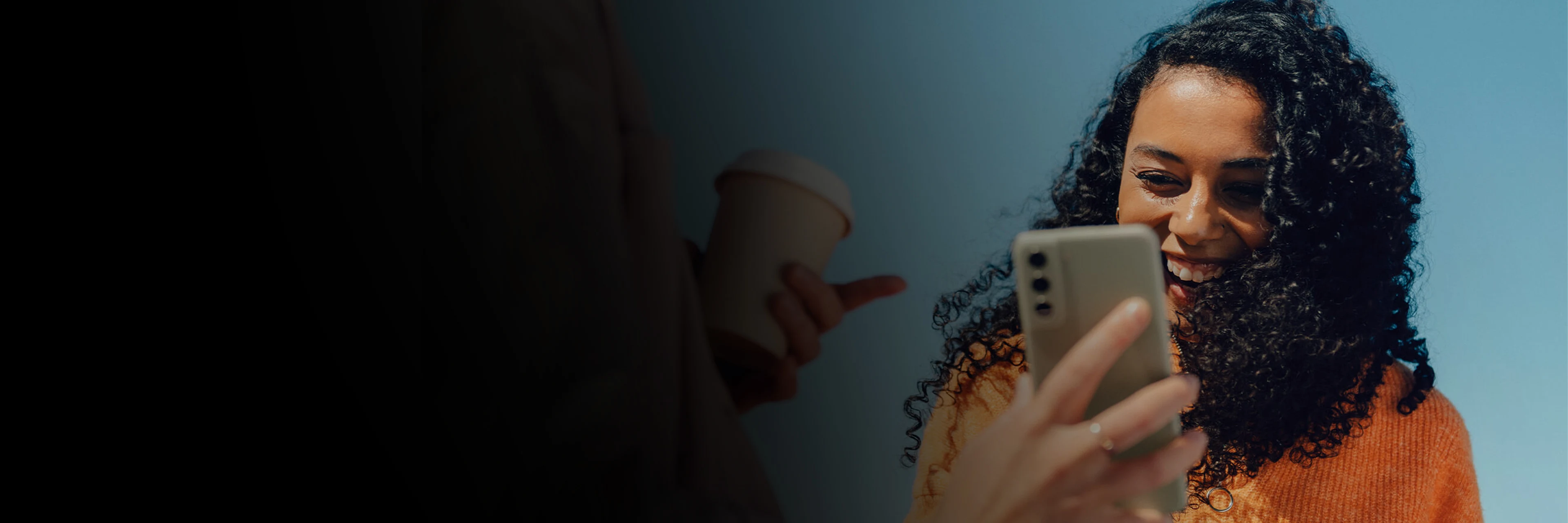 Leende kvinna tittar på mobil, någon håller kaffekopp