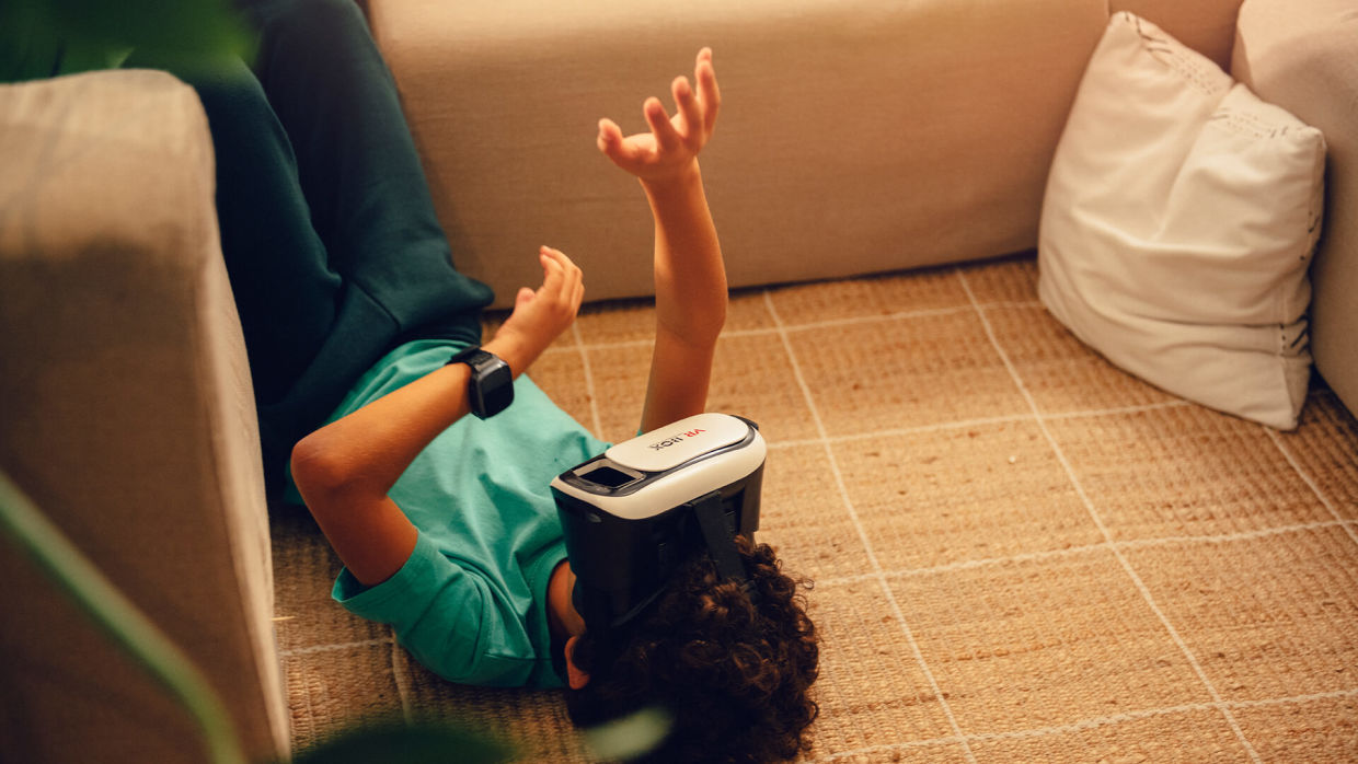 Ett barn med grön tröja ligger på golvet med VR-glasögon på sig.