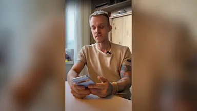 En kille i ljus tröja sitter och tittar på en mobil.