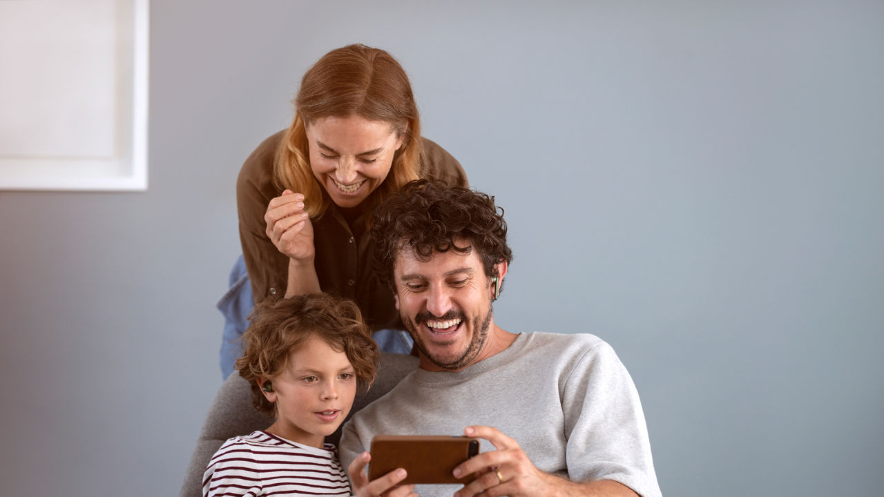 Tre personer tittar på en mobiltelefon. De har roligt för alla ser glada ut.