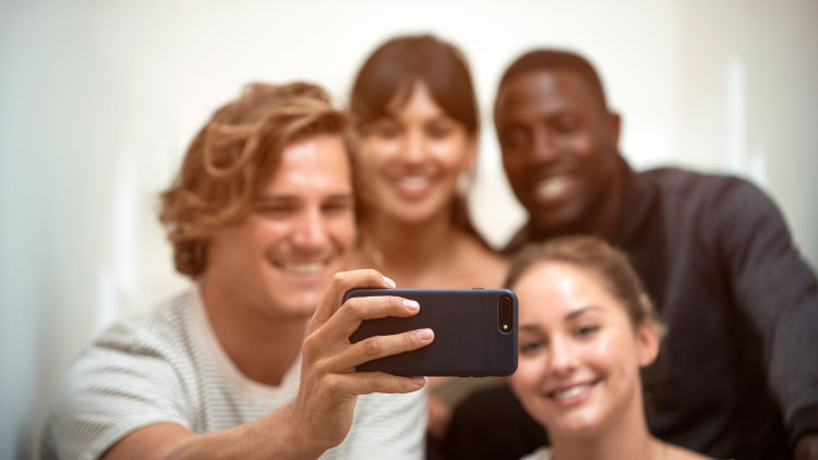 Kompisgäng bestående av två killar och två tjejer tar en groupie/selfie med en mobil.