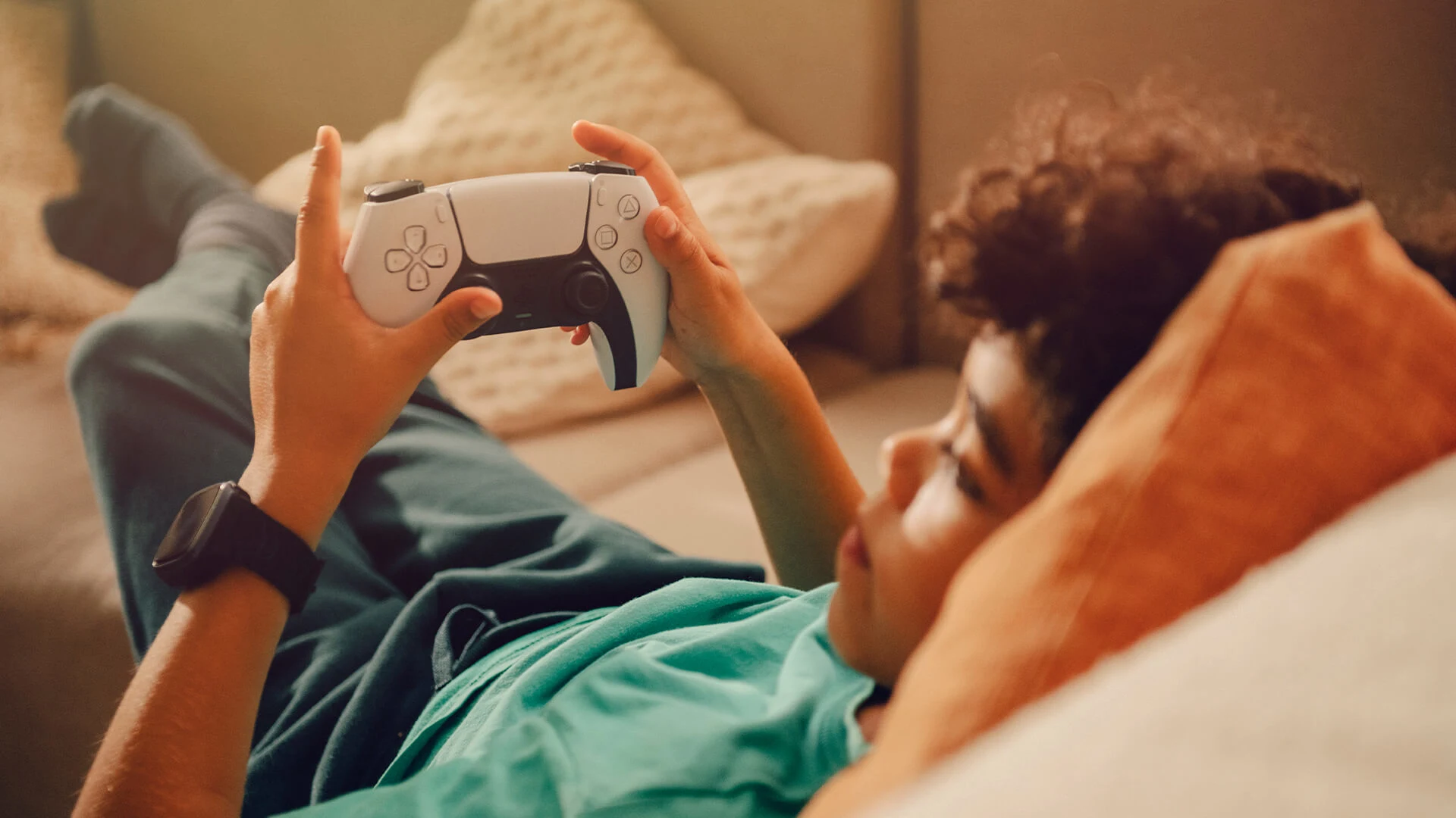 Barn ligger i soffan och gamear med en trådlös handkontroll