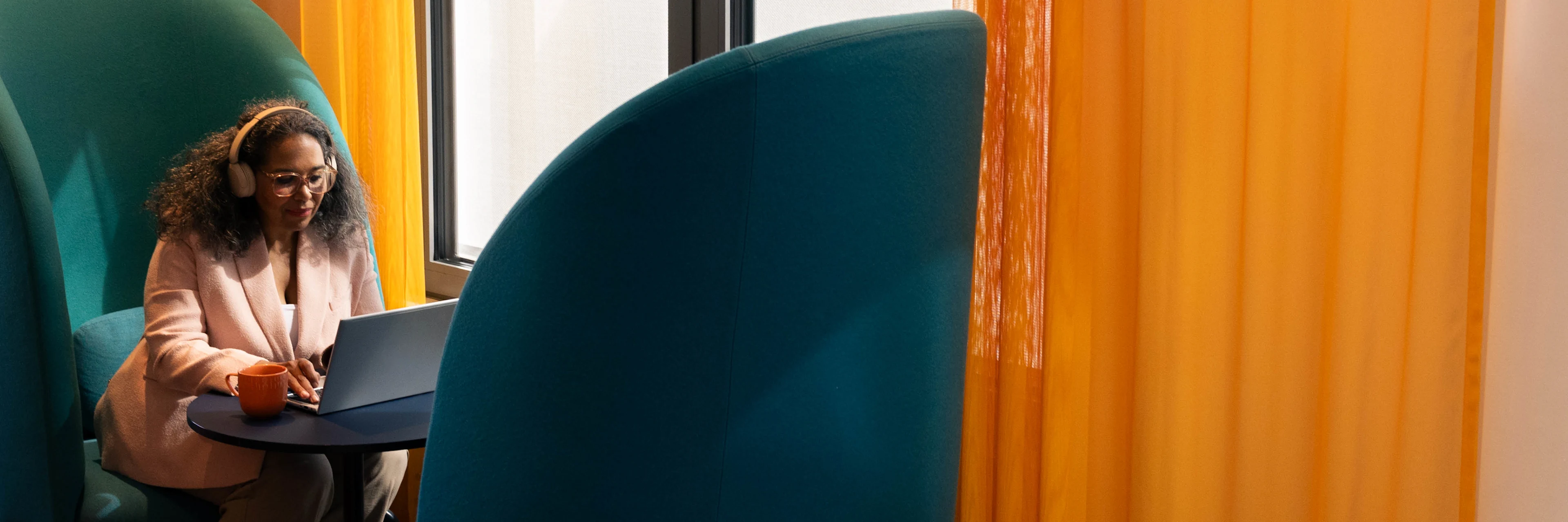 En kvinna sitter i en stor blå fåtölj och jobbar på sin laptop