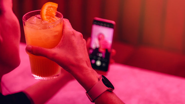 En hand håller i en mobil mot en orange bakgrund.