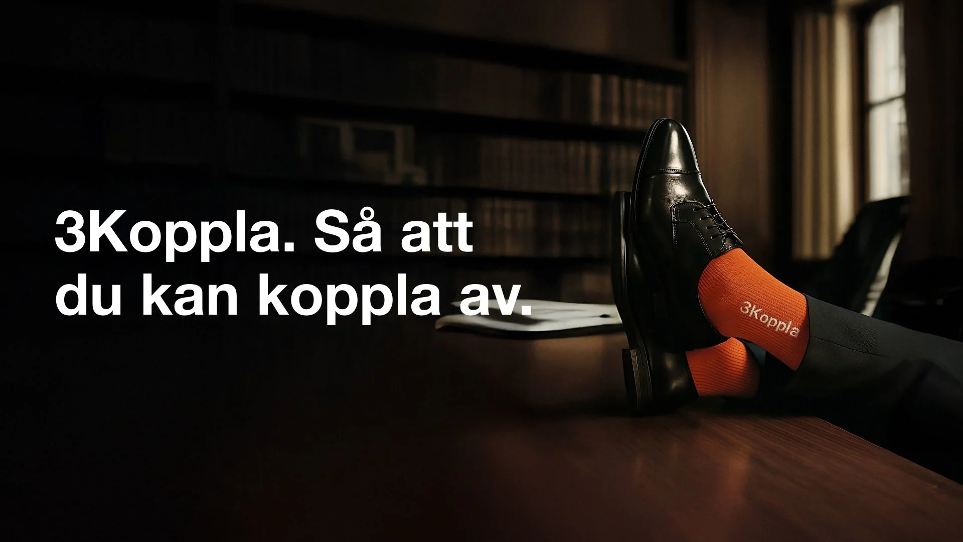 En person i kostym med fötterna på bordet, bär svarta skor och orange strumpor med texten "3koppla" på i vitt. På den vänstra sidan i bilden står texten: "Det finaste man kan ge är lite mer".