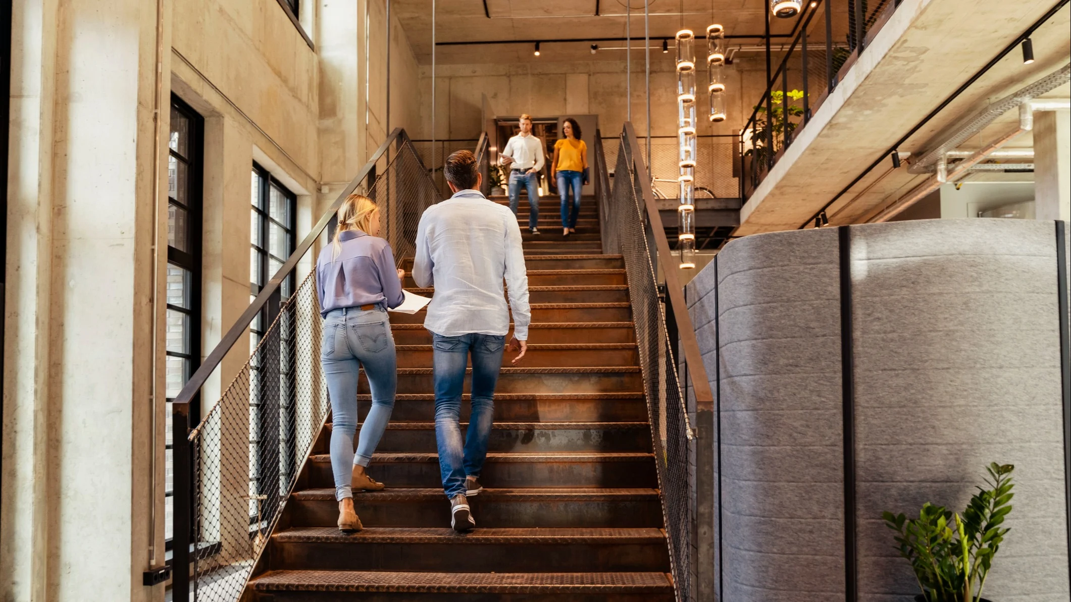 Fyra personer går upp och ner för en trappa i ett modernt, ljust kontorsutrymme med betongväggar.
