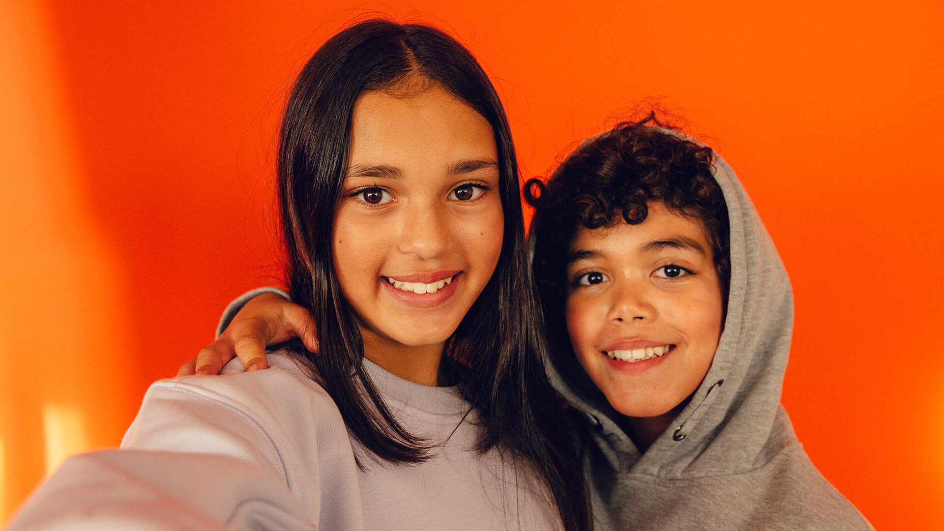 Två barn ler mot kameran mot orange bakgrund.