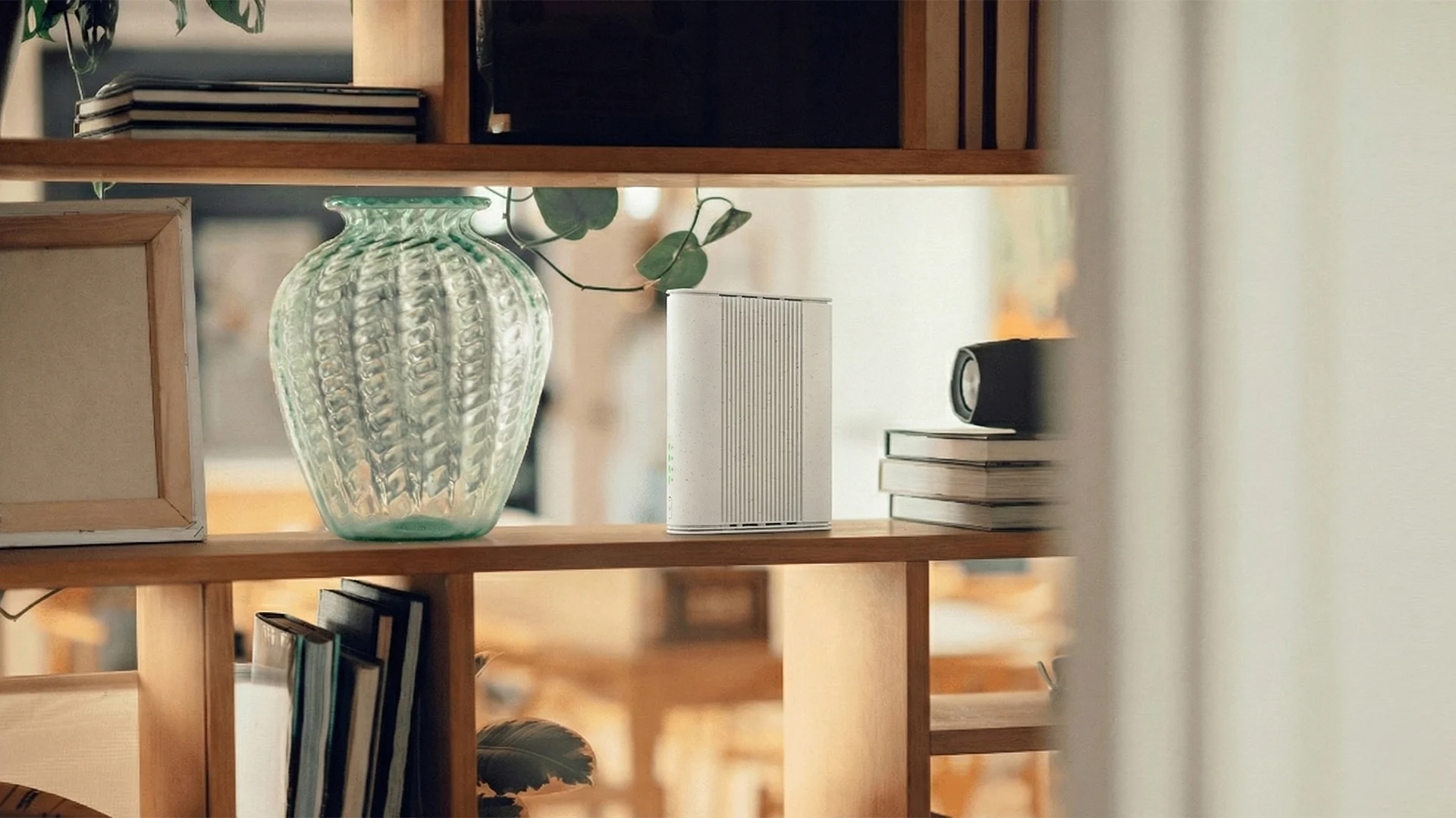 A wooden shelf with a router, books, and a small speaker, set against a blurred background.