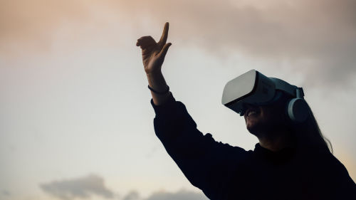Tjej med VR-glasögon håller upp handen framför sig.