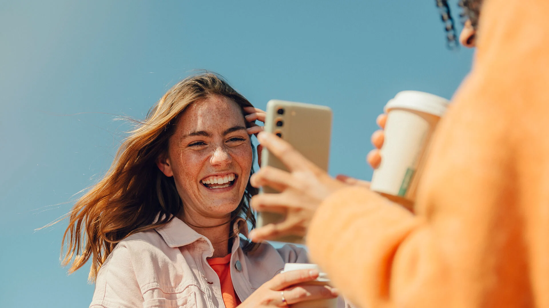 En kvinna visar upp något på sin mobil för sin kompis, båda skrattar.