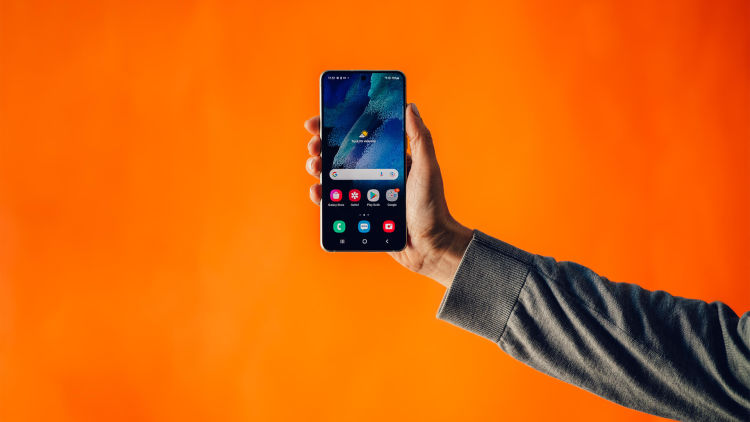 En hand håller i en mobil mot en orange bakgrund.