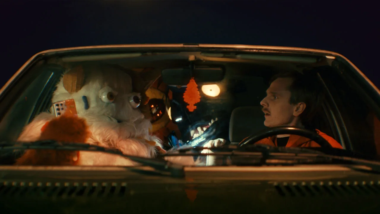 En man tillsammans med två gulliga monster sitter i en bil.