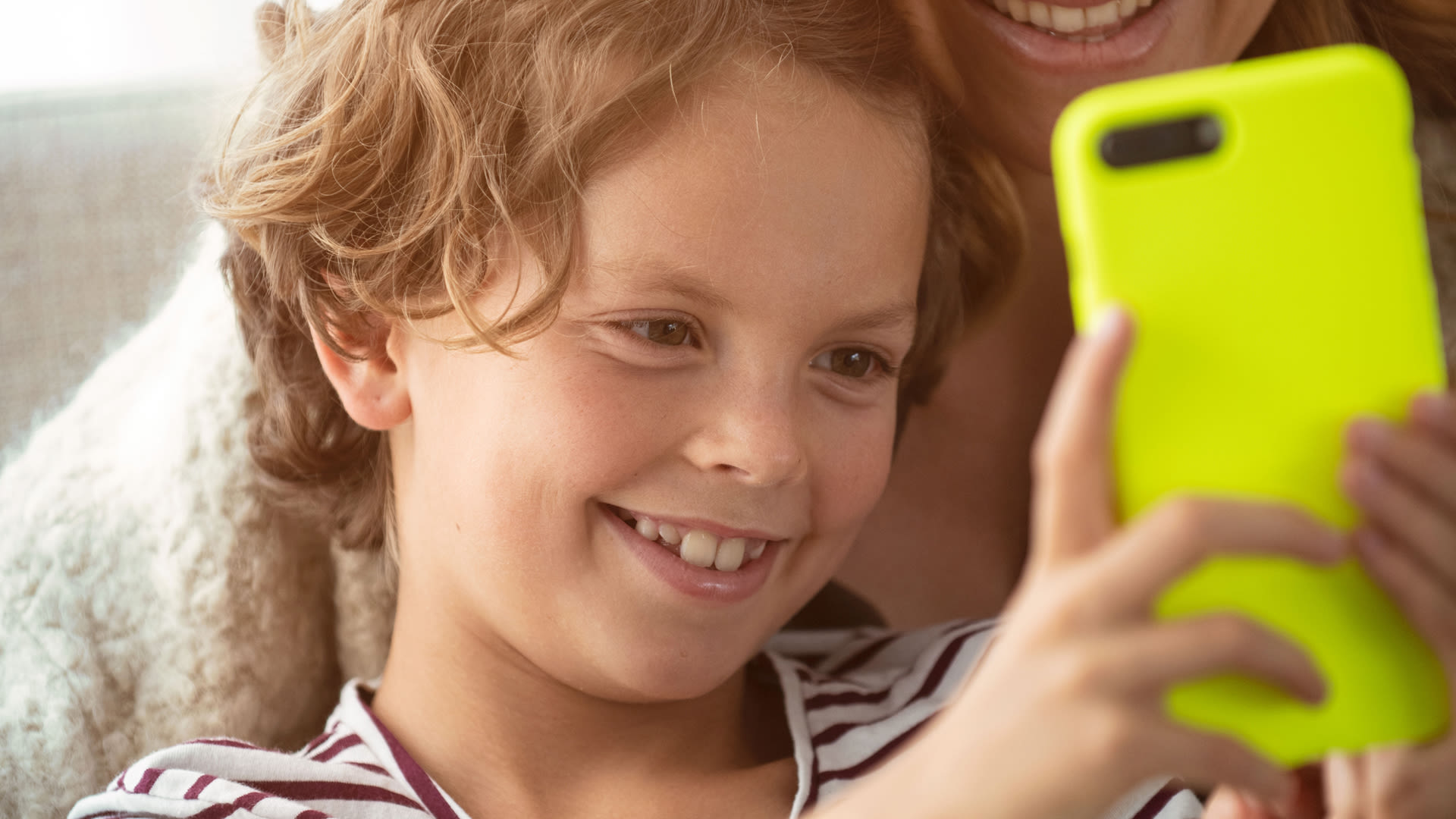Ett barn håller upp en mobil och tittar på den. Barnet ler.