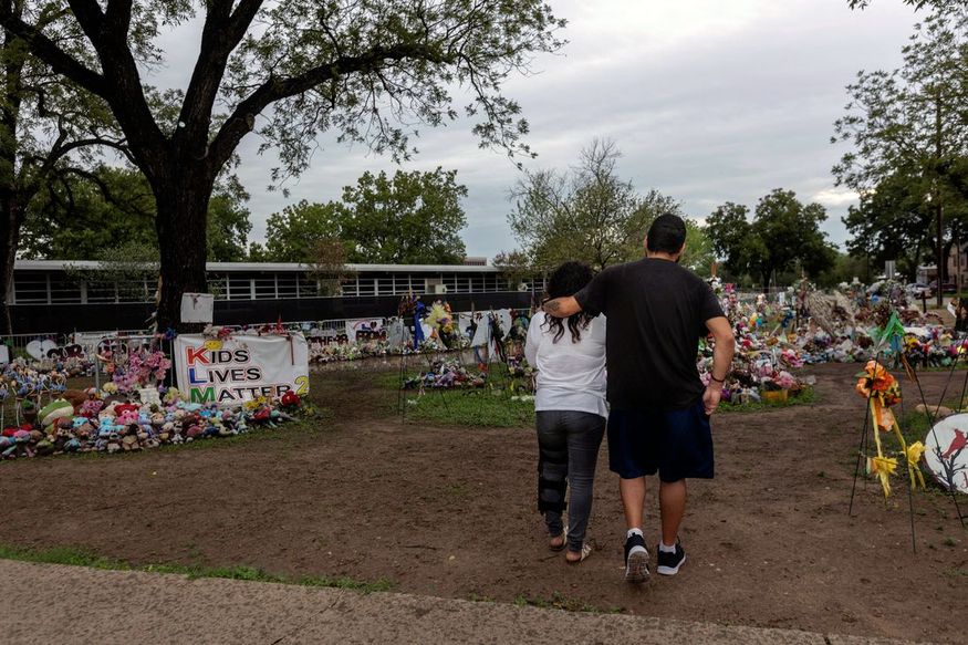 A man hugs a woman as they walk towards a memorial outside of Robb Elementary School in Uvalde, TX
