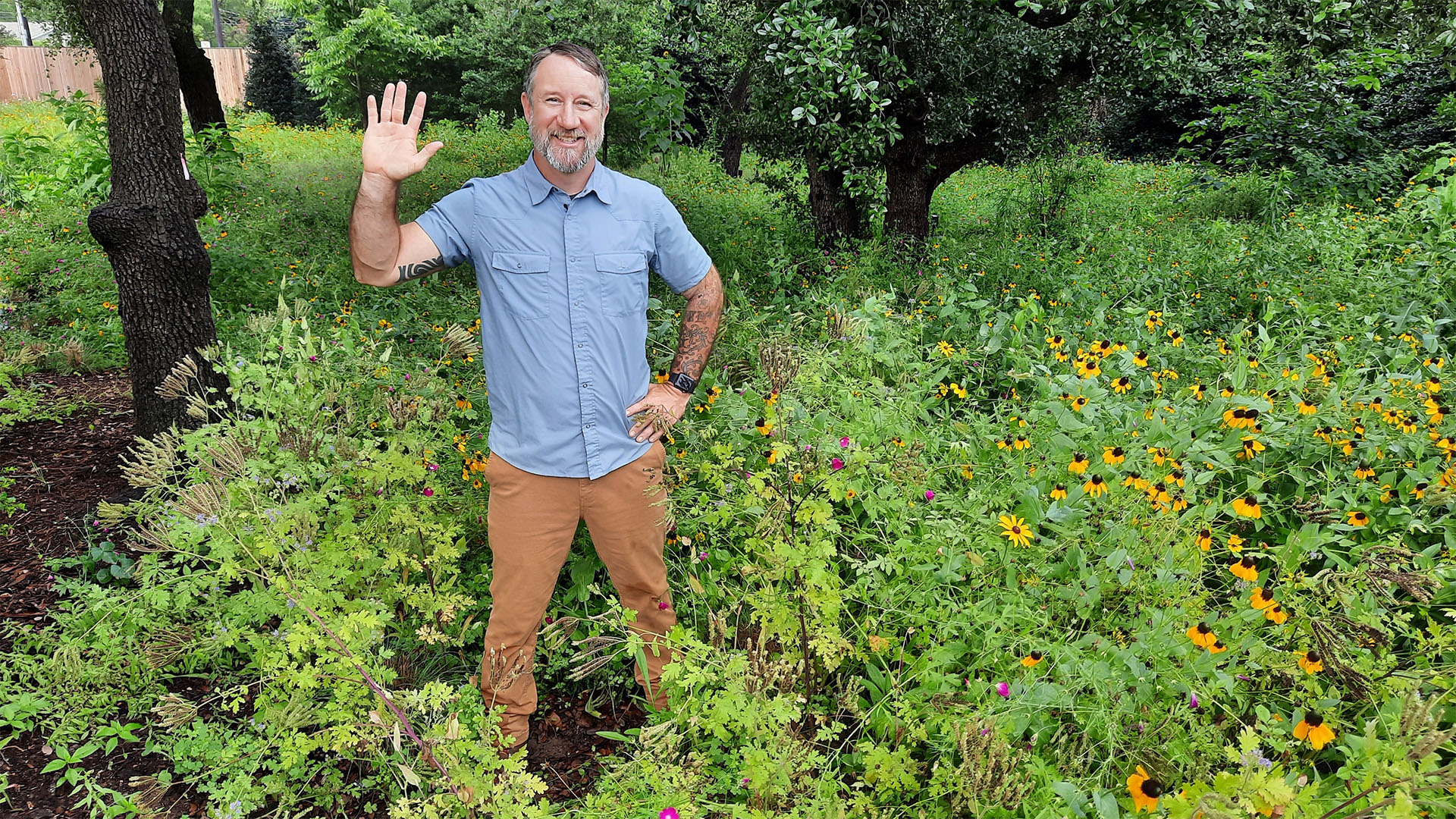CTG host John Hart Asher wearing a blue shirt and brown trousers standing in Texas wildflowers