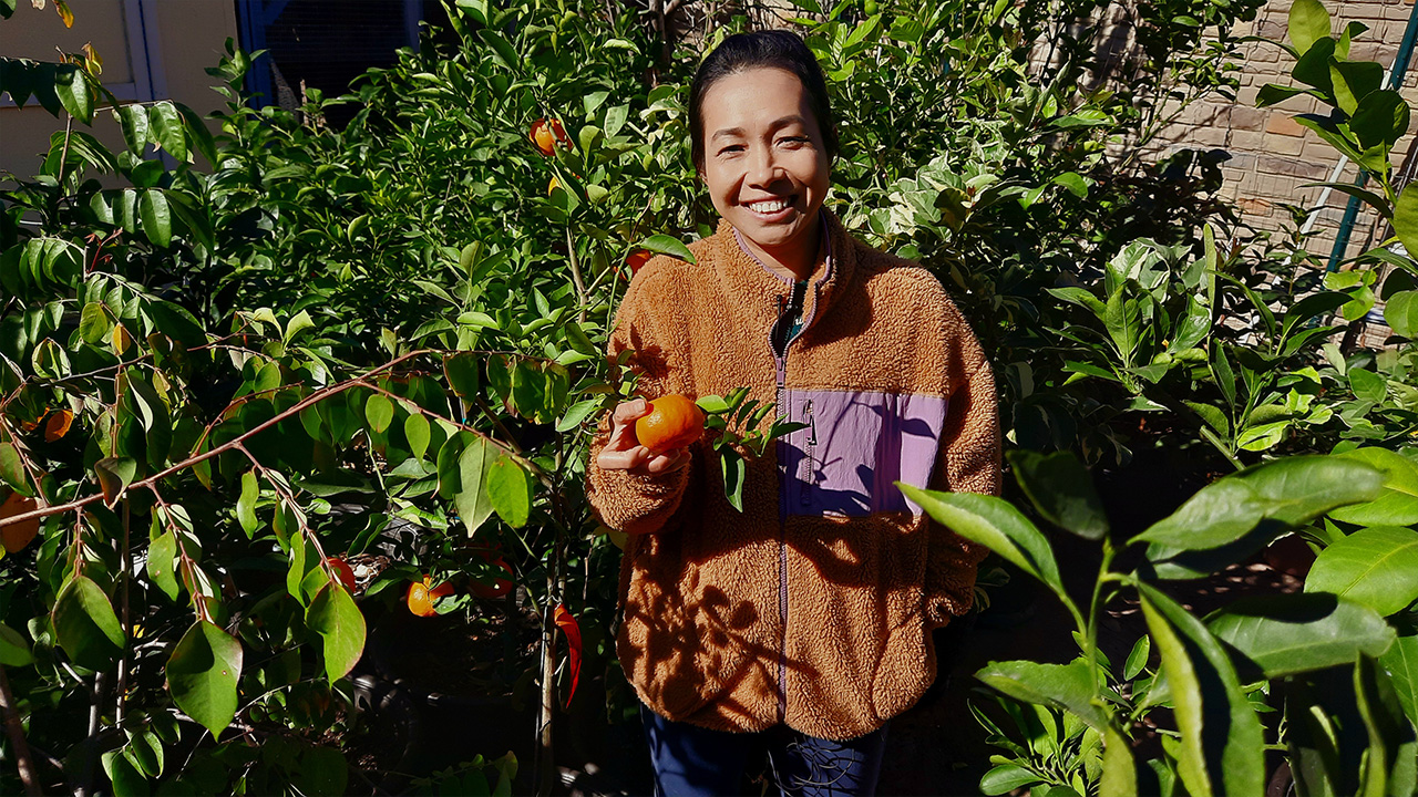 A woman in a brown sweatshirt holds a tangerine