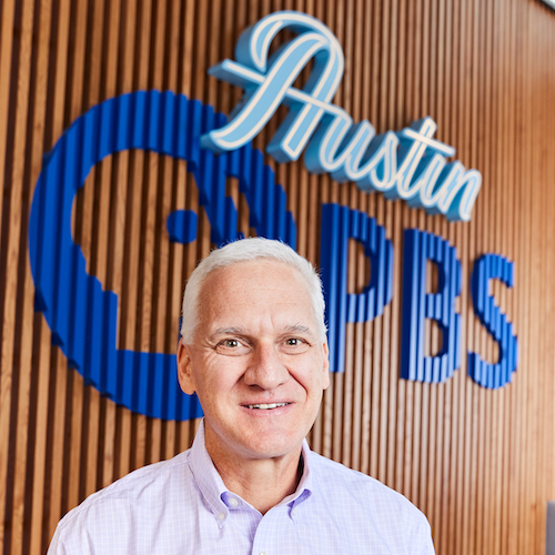 Benjamin Kramer, Ph.D. Chief Education Officer in front of the Austin PBS logo