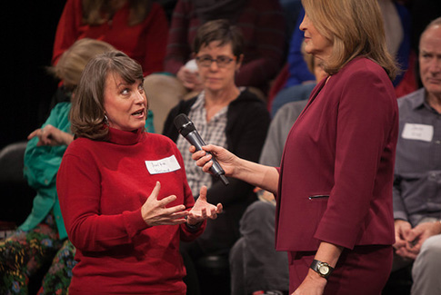 Judy Maggio holding a microphone up to an audience member who is speaking, during an ATX Together town hall taping in Studio 6A.