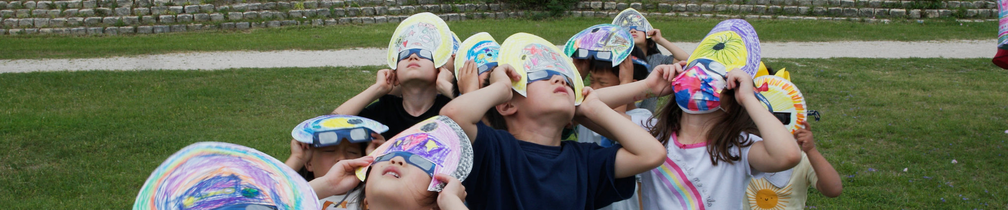 A group of elementary students wearing eclipse glasses looking up at the sky.
