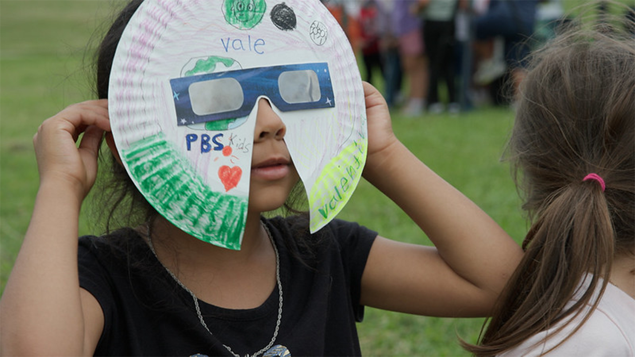 A child watches the solar eclipse using eclipse glasses