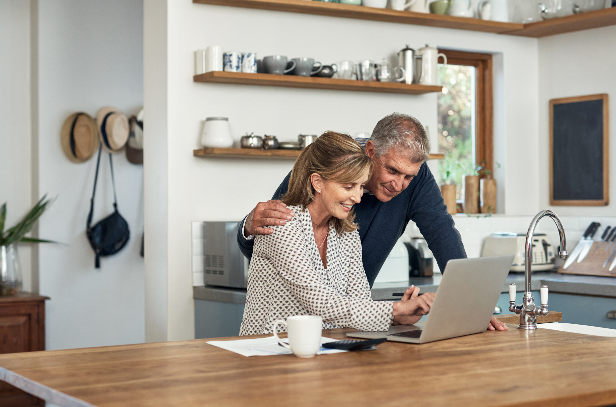 A senior couple planning their finance and paying bills while using a laptop at home. A mature man and woman going through paperwork and working online with a computer