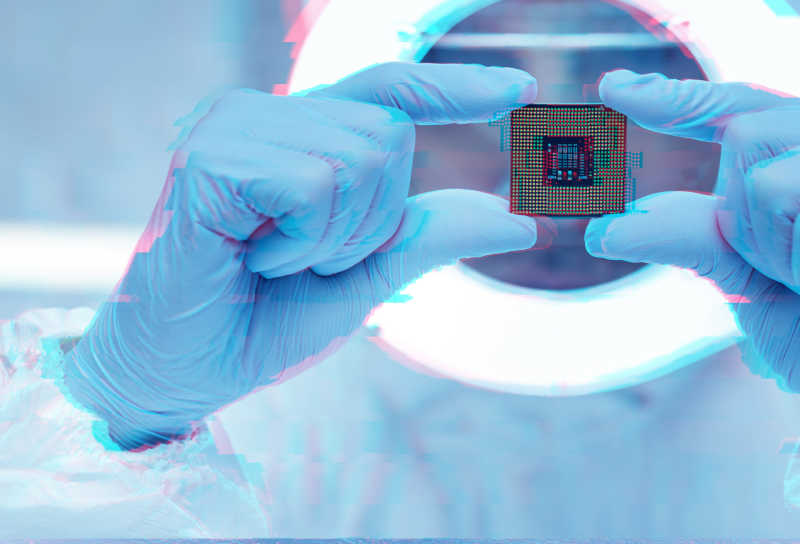 A digitized image of a person wearing nitrile gloves holds a computer chip under a light. 