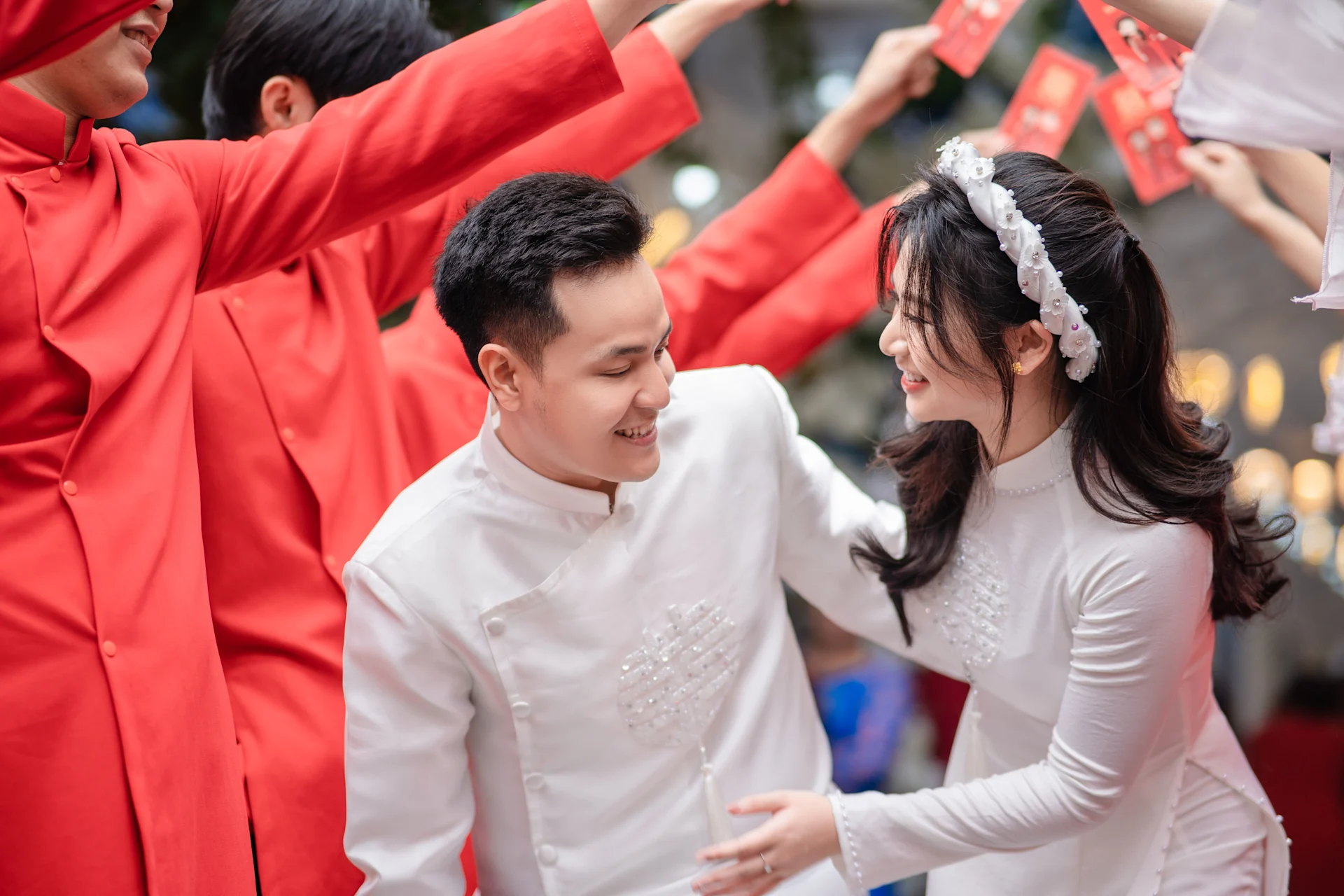 A Vietnamese wedding couple, with the bride in a white áo dài and wearing a modern headband-style khăn đóng. Source: https://www.pexels.com/photo/newlywed-passing-under-the-tunnel-of-wedding-guests-arms-19476300/