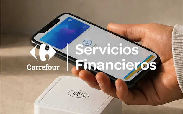 Logo de Carrefour Banco sobre una mano que sostiene un celular encima de una terminal de pago