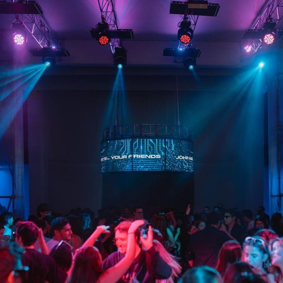 Imagen de discoteca, gente bailando , luces azules y violetas. De fondo la cabina del DJ a altura