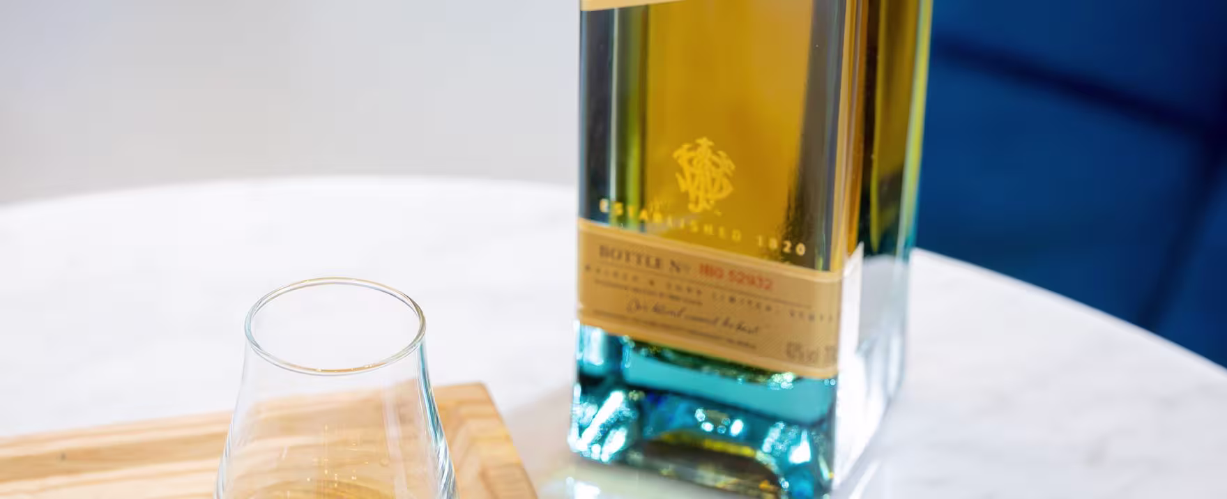 La imagen muestra una botella de whisky Johnnie Walker Blue Label junto a un vaso que contiene este destilado, con un chocolate ubicado a un lado.