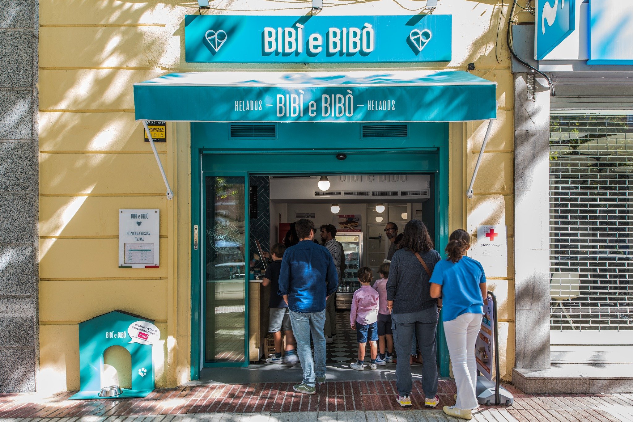 Fachada de Bibi e Bibò Príncipe de Vergara con toldo turquesa, entrada animada y zona para mascotas junto a la puerta.