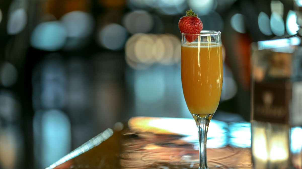 A Bucks Fizz cocktail in a flute next to a bottle of Champagne 
